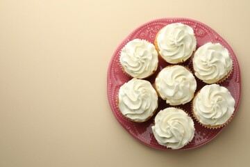 Tasty vanilla cupcakes with cream on beige background, top view. Space for text