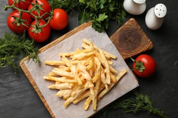 Delicious French fries with cheese sauce, tomatoes, dill and parsley on black table, flat lay