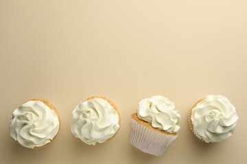 Tasty vanilla cupcakes with cream on beige background, top view. Space for text