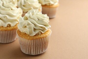 Tasty vanilla cupcakes with cream on beige table, closeup. Space for text