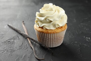 Tasty cupcake with cream and vanilla pods on black table, closeup