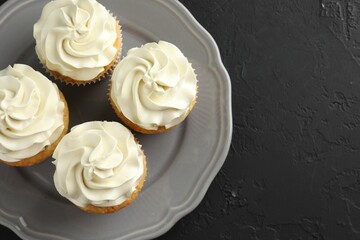 Tasty cupcakes with vanilla cream on black table, top view. Space for text