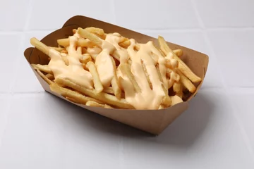 Poster Delicious French fries with cheese sauce on white tiled table, closeup © New Africa