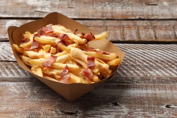 Keuken spatwand met foto Tasty potato fries, cheese sauce and bacon in paper container on wooden table, closeup. Space for text © New Africa