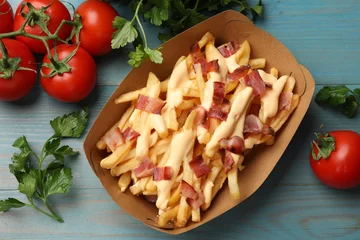 Fotobehang Tasty potato fries, cheese sauce, bacon and products in paper container on light blue wooden table, top view © New Africa