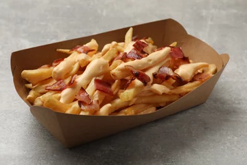 Raamstickers Tasty potato fries, cheese sauce and bacon in paper container on grey table, closeup © New Africa