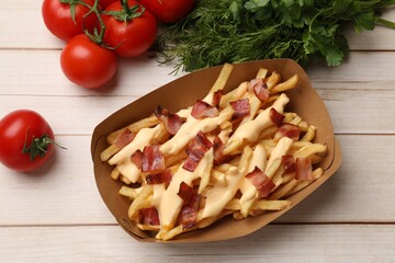 Tasty potato fries, cheese sauce, bacon and products in paper container on light wooden table, top view