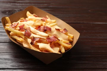 Keuken spatwand met foto Tasty potato fries, cheese sauce and bacon in paper container on wooden table, closeup © New Africa