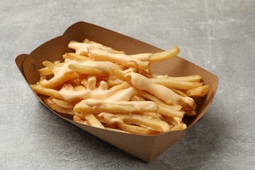 Tasty potato fries and cheese sauce in paper container on grey table, closeup