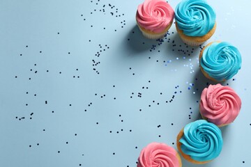 Delicious cupcakes with bright cream and confetti on light blue background, flat lay. Space for text