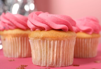 Delicious cupcakes with bright cream and confetti on pink table, closeup