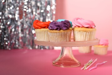 Delicious cupcakes with bright cream and candles on pink table, space for text