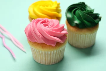 Rolgordijnen Delicious cupcakes with bright cream on turquoise background, closeup © New Africa