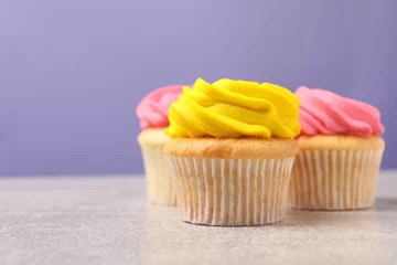 Gordijnen Delicious cupcakes with bright cream on gray table against violet background, space for text © New Africa