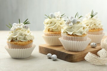 Tasty Easter cupcakes with vanilla cream and candies on gray table