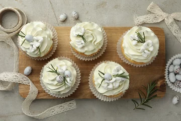  Tasty Easter cupcakes with vanilla cream, candies and ribbon on gray table, flat lay © New Africa