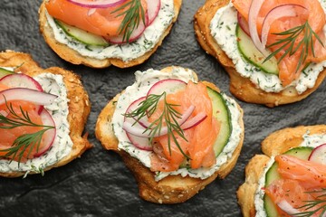 Tasty canapes with salmon, cucumber, radish and cream cheese on slate board, top view