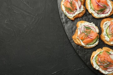 Tasty canapes with salmon, cucumber, radish and cream cheese on black table, top view. Space for...