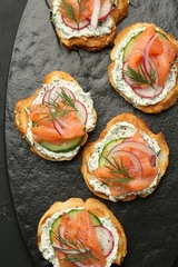 Fotobehang Tasty canapes with salmon, cucumber, radish and cream cheese on black table, top view © New Africa