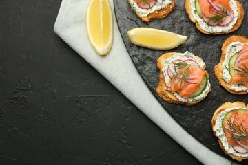  Tasty canapes with salmon, cucumber, radish and cream cheese on black table, top view. Space for text © New Africa