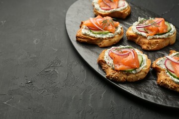 Tasty canapes with salmon, cucumber, radish and cream cheese on black table, space for text