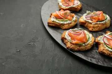 Gordijnen Tasty canapes with salmon, cucumber, radish and cream cheese on black table, space for text © New Africa