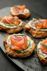 Tasty canapes with salmon, cucumber, radish and cream cheese on black table, closeup