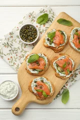 Gordijnen Tasty canapes with salmon, capers, cucumber and sauce on white wooden table, top view © New Africa