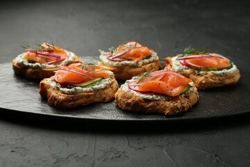 Tasty canapes with salmon, cucumber, radish and cream cheese on black table
