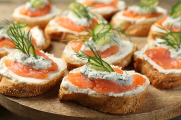 Tasty canapes with salmon, cucumber, cream cheese and dill on wooden stand, closeup