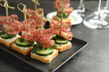 Rolgordijnen Tasty canapes with salami, cucumber and cream cheese on grey table, closeup. Space for text © New Africa