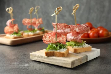 Gordijnen Tasty canapes with salami, greens and cream cheese on grey table, closeup © New Africa