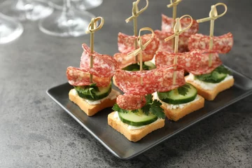 Raamstickers Tasty canapes with salami, cucumber and cream cheese on grey table © New Africa