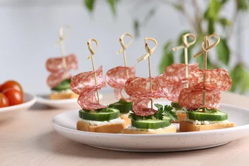 Poster Tasty canapes with salami, cucumber and cream cheese on light table, closeup © New Africa