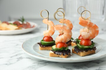 Tasty canapes with shrimps, cucumber, greens and tomatoes on white marble table, closeup