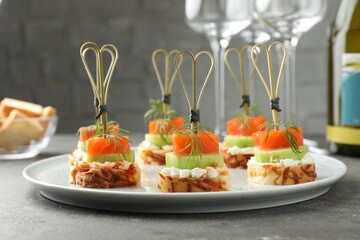 Tasty canapes with salmon, cucumber, bread and cream cheese on grey table