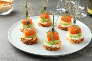 Tasty canapes with salmon, cucumber, bread and cream cheese on grey table