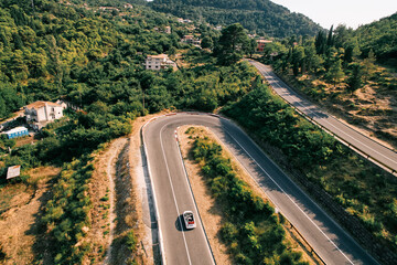 Fototapeta na wymiar White convertible is driving along a serpentine road in the mountains. Drone