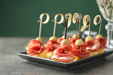 Tasty canapes with olives, prosciutto and cheese on grey table, closeup