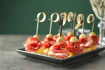 Plexiglas foto achterwand Tasty canapes with olives, prosciutto and cheese on grey table, closeup © New Africa