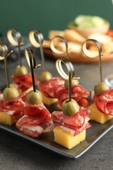 Tasty canapes with olives, prosciutto and cheese on grey table, closeup - obrazy, fototapety, plakaty