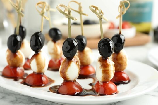 Tasty canapes with black olives, mozzarella and cherry tomatoes on white marble table, closeup