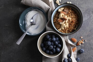Tasty granola in bowl, blueberries, yogurt and spoon on gray textured table, flat lay