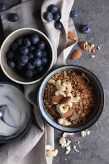 Gordijnen Tasty granola in bowl, blueberries and yogurt on gray textured table, flat lay © New Africa