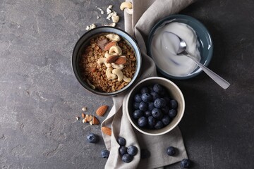 Tasty granola in bowl, blueberries, yogurt and spoon on gray textured table, flat lay. Space for...