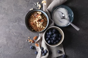 Poster Tasty granola in bowl, blueberries, yogurt and spoon on gray textured table, flat lay. Space for text © New Africa