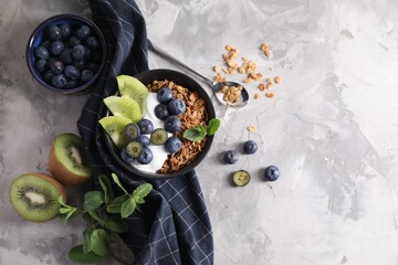Tasty granola with yogurt, blueberries and kiwi in bowl on gray textured table, flat lay. Space for text