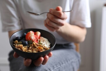 Woman eating tasty granola with berries, yogurt and seeds indoors, closeup