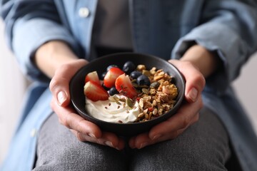 Woman holding bowl of tasty granola with berries, yogurt and seeds, closeup
