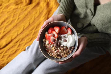 Fotobehang Woman holding bowl of tasty granola with chocolate chips, strawberries and yogurt indoors, top view © New Africa